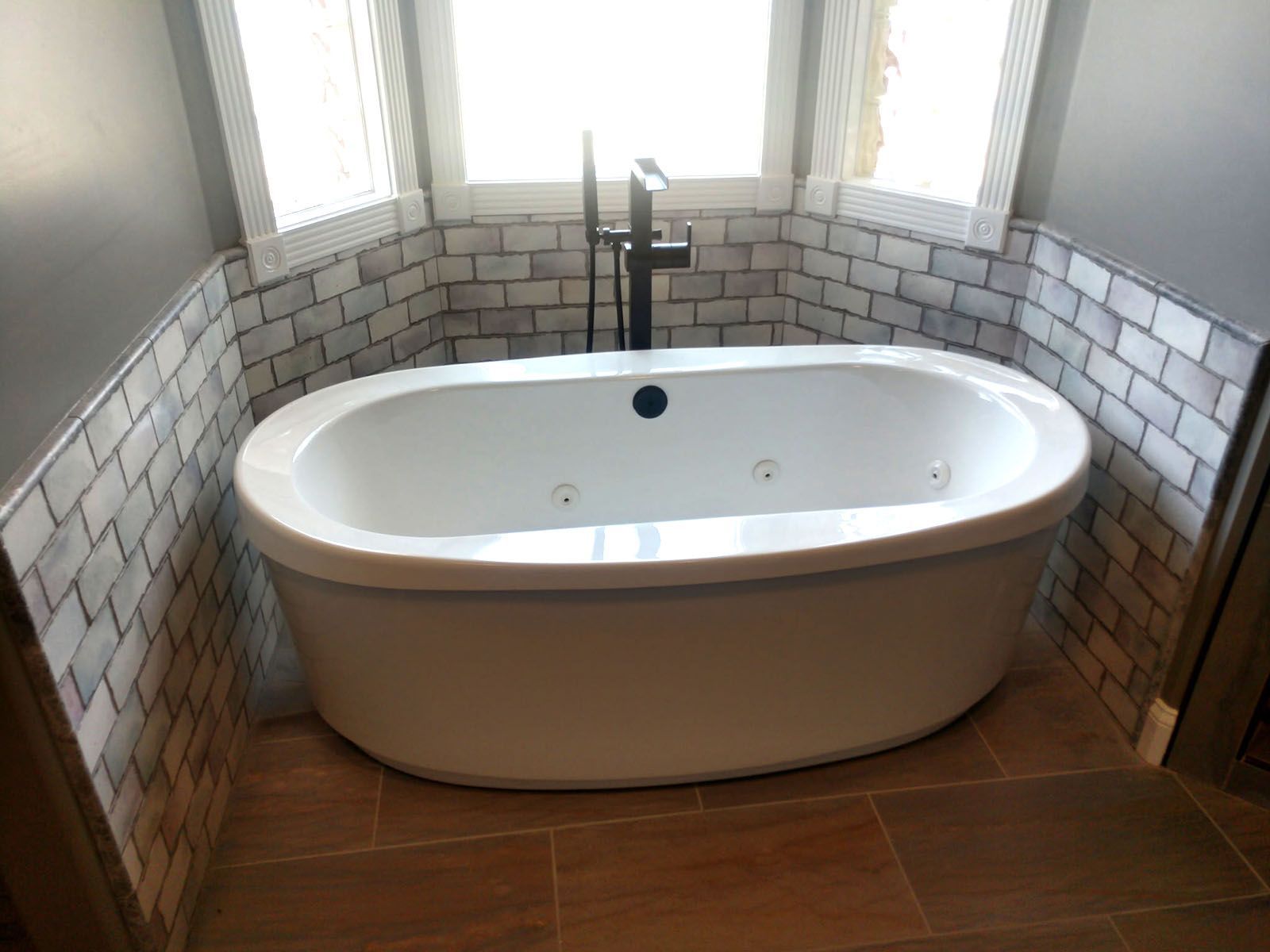 A deep white bathtub is sitting in a bathroom next to a window