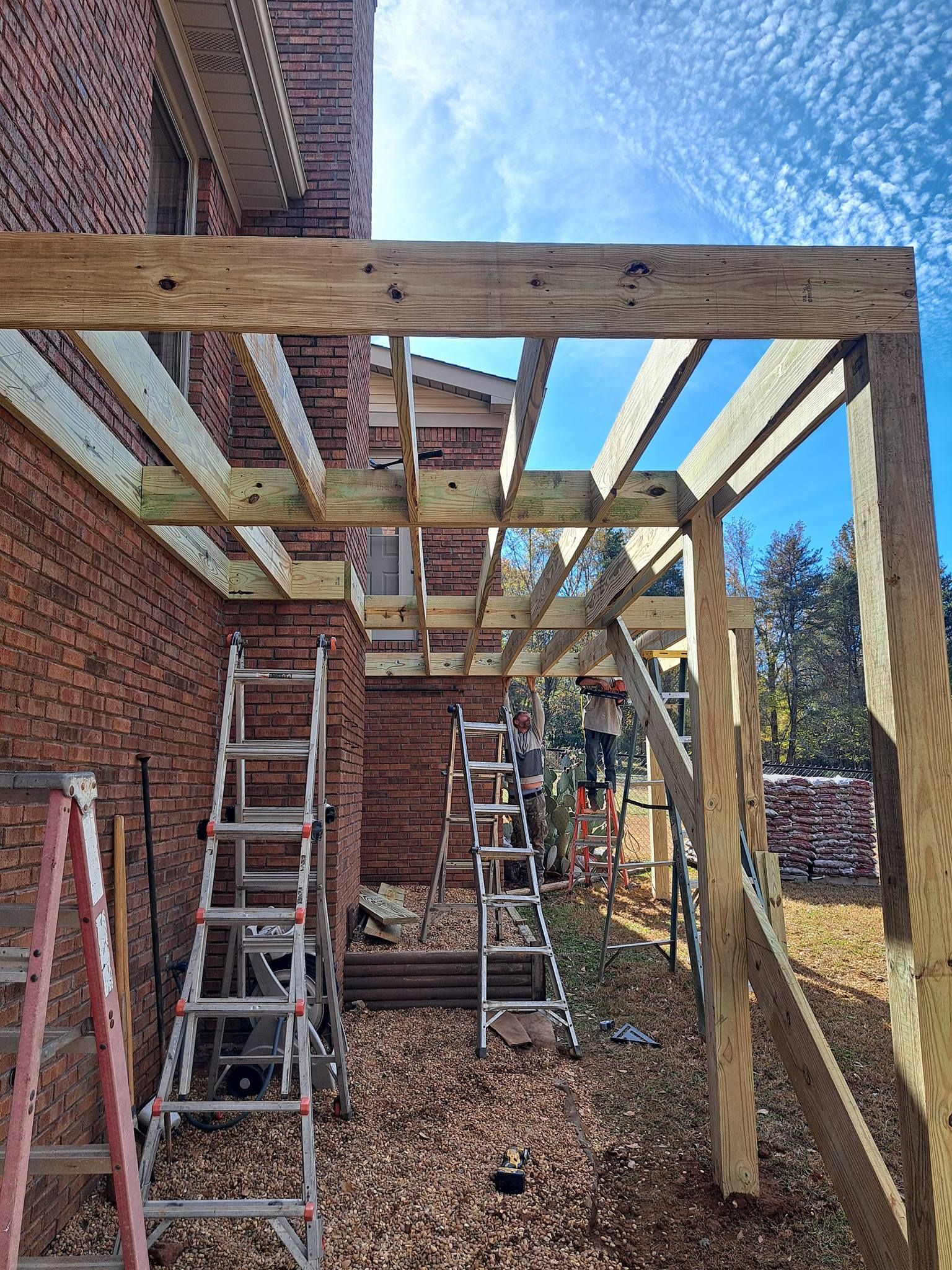 Construction of a wooden pergola attached to a brick building; ladders and tools visible.