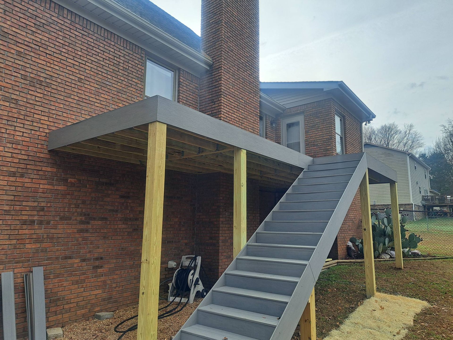 Deck with stairs attached to a brick building. Gray deck boards, light brown support beams.