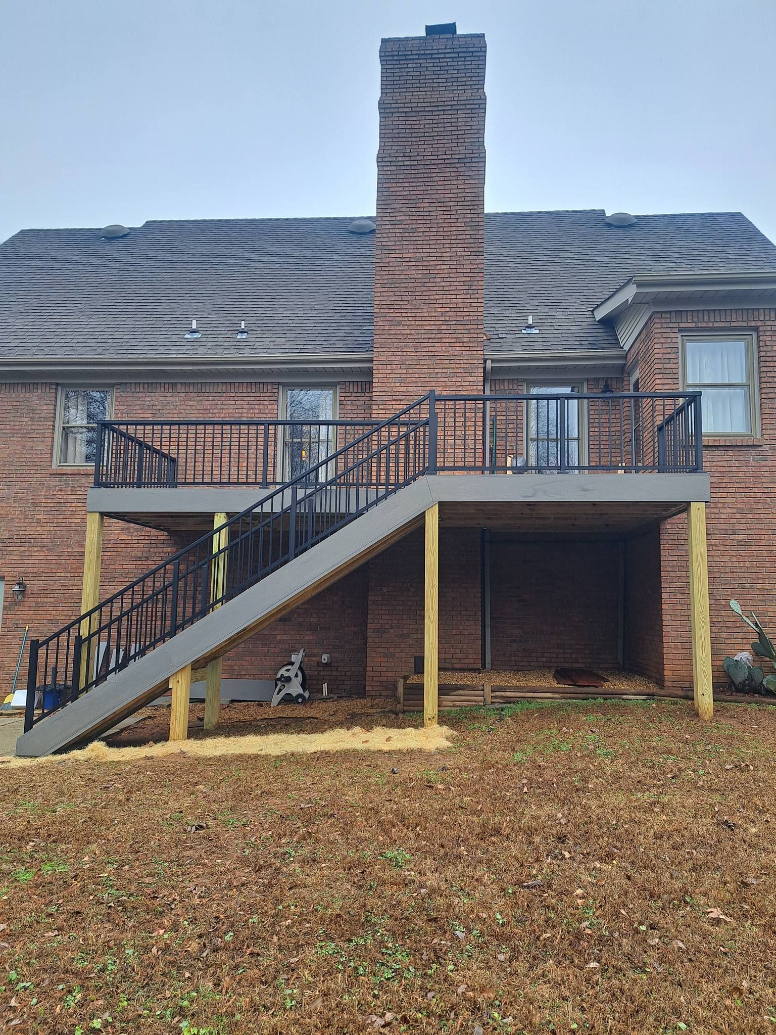 A multi-level wooden deck with stairs attached to a brick house with a chimney.