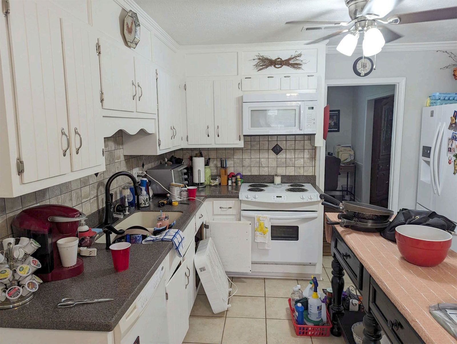An old kitchen with white cabinets, a stove, a microwave, and a ceiling fan