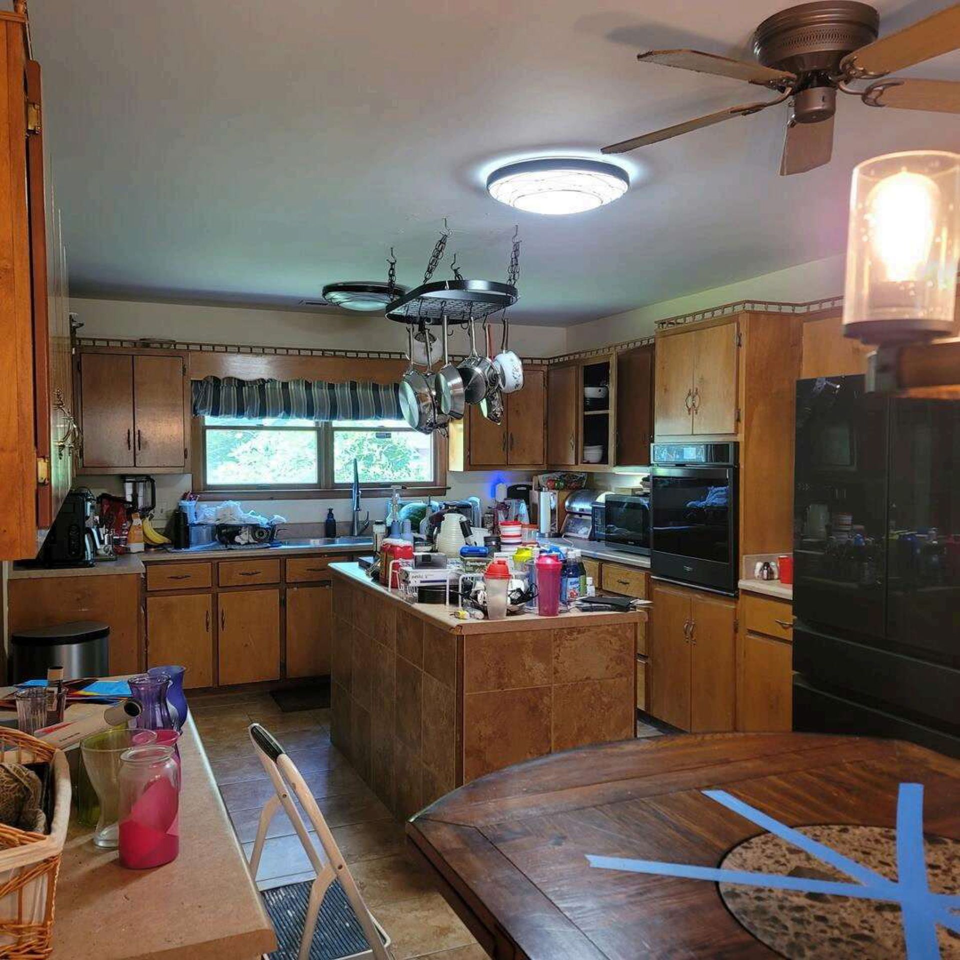 Kitchen with wooden cabinets, an island, and a dining table; full of cooking supplies.