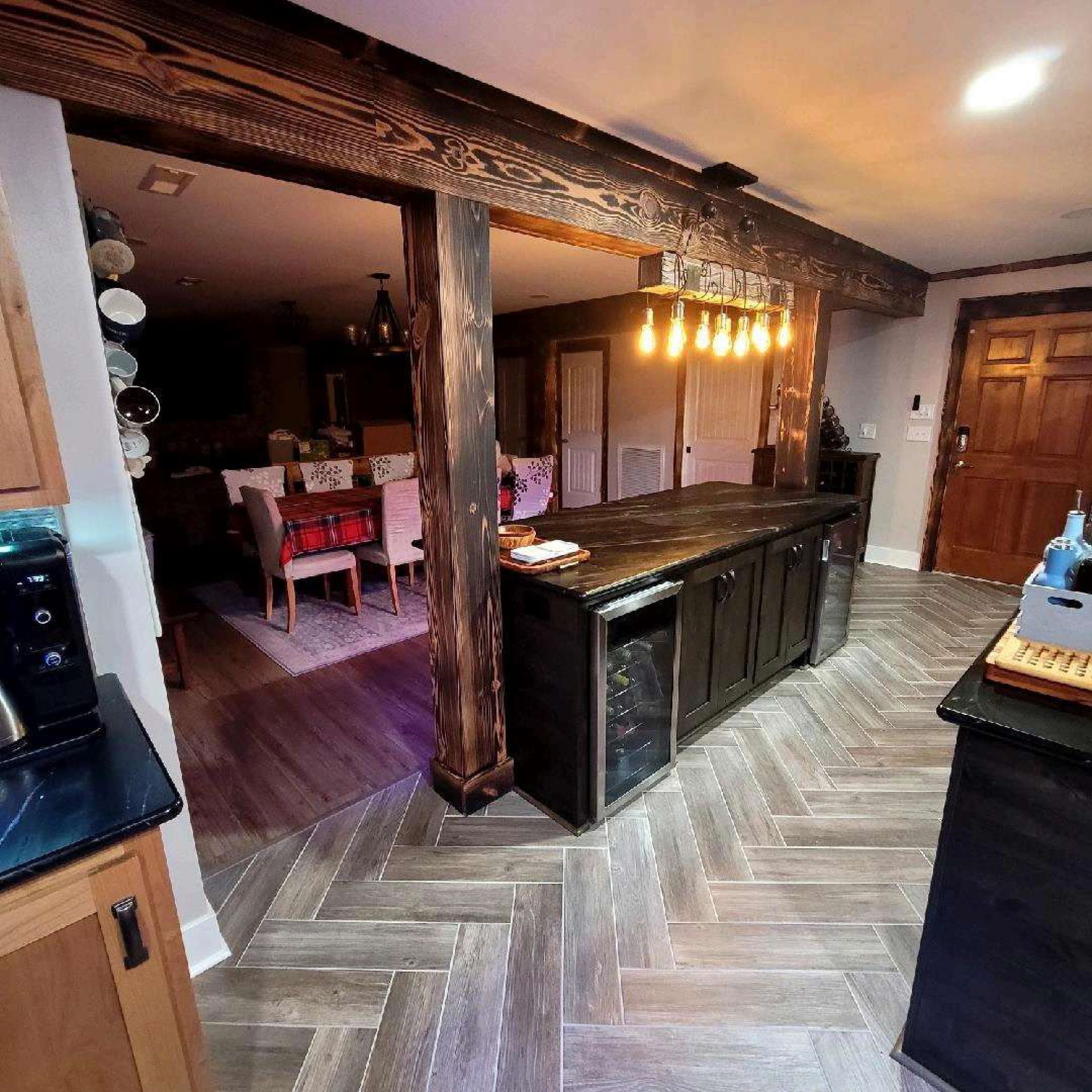 Kitchen with dark wood beams, island, and dining area visible. Herringbone floors, neutral tones.