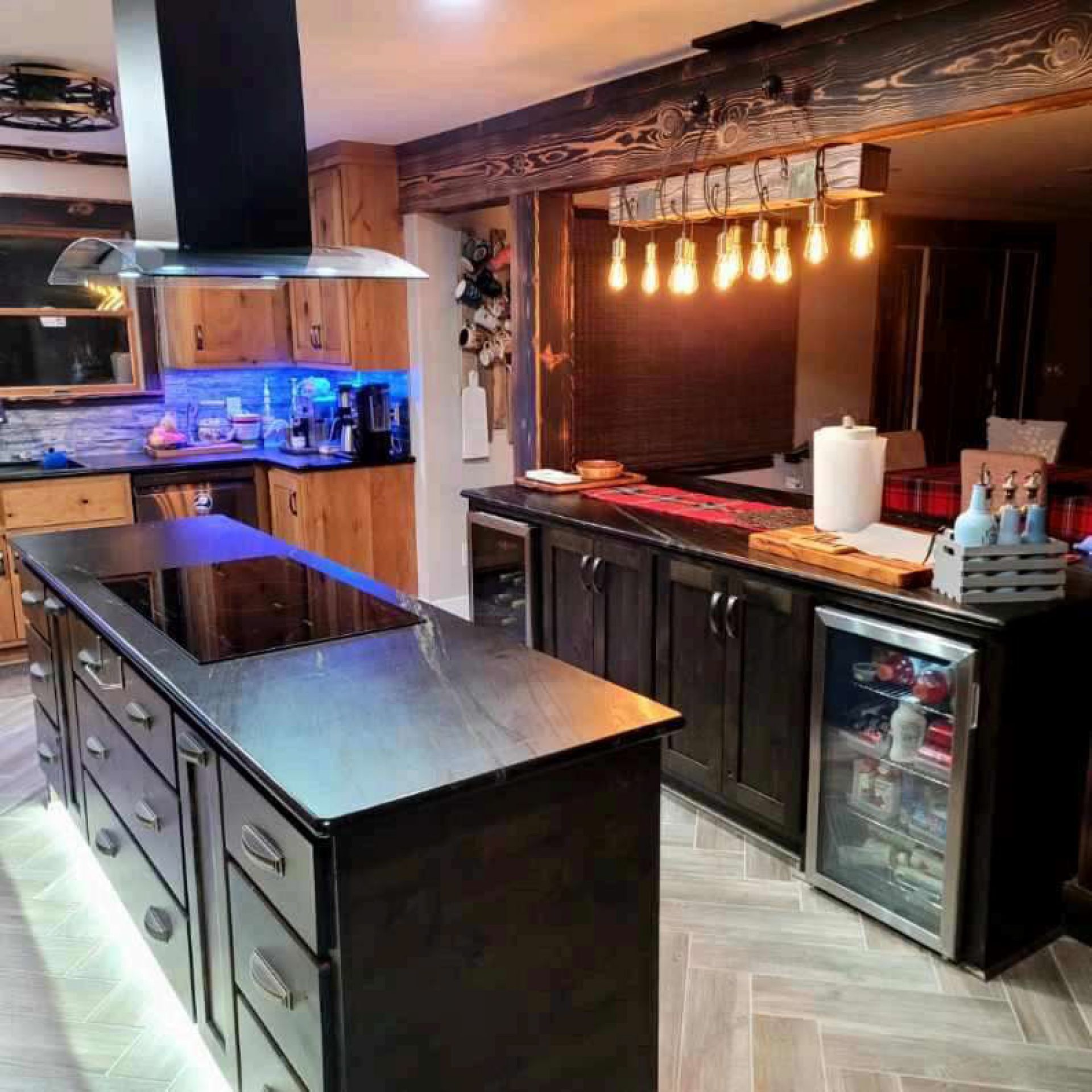 Rustic kitchen with two islands, dark cabinetry, stainless steel appliances, and warm lighting.
