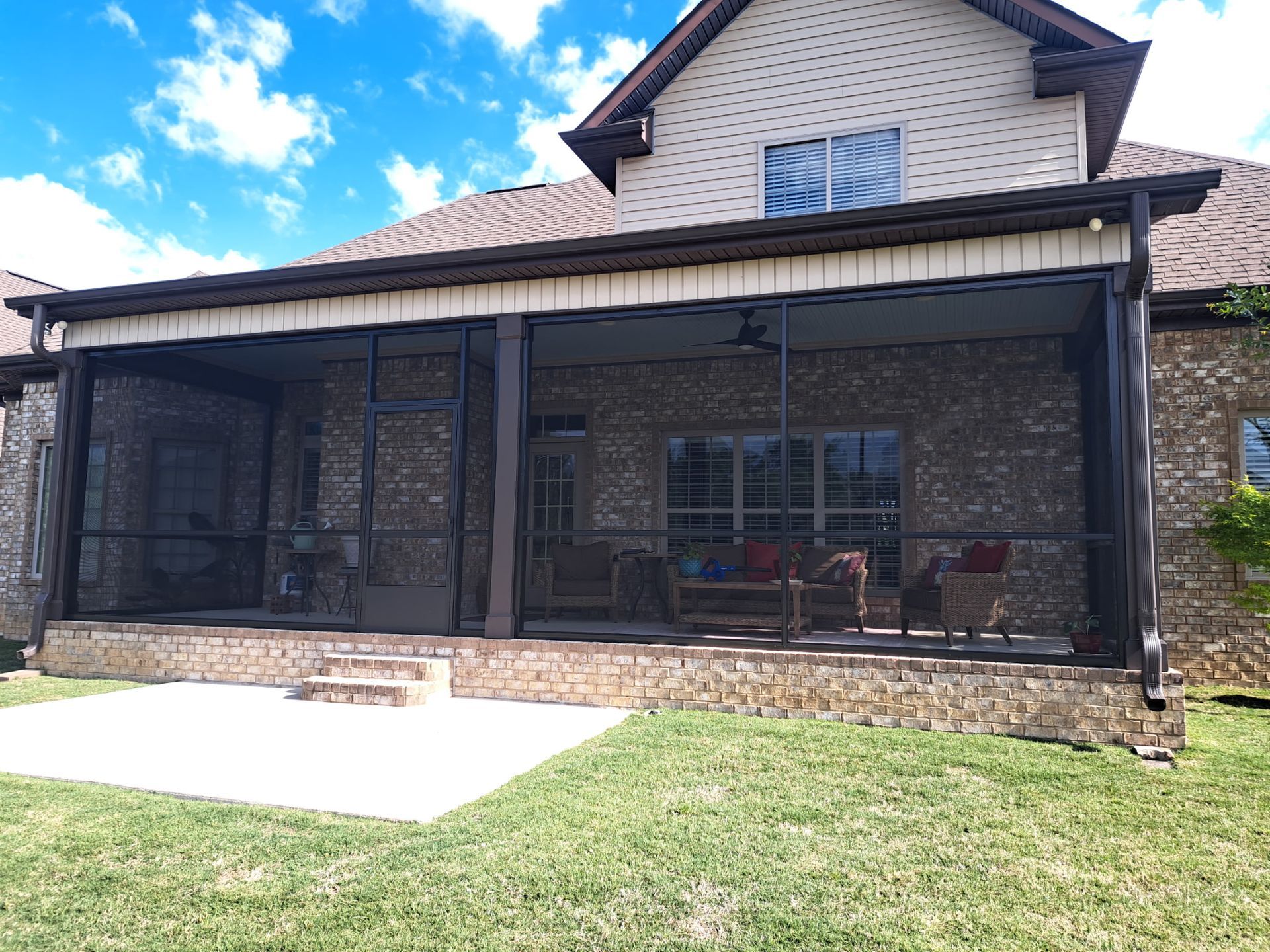 Covered stone patio with screened enclosure attached to a two-story house and lawn in front
