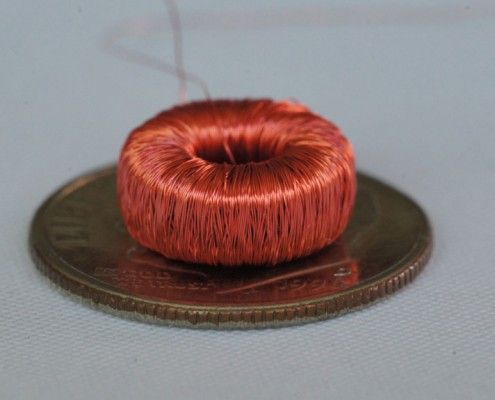 A copper wire coil is sitting on top of a penny.