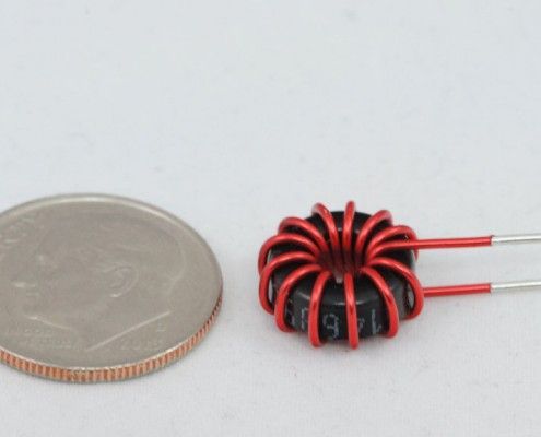 A small red wire coil is next to a quarter
