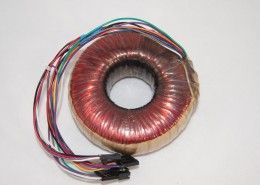 A close up of a toroidal transformer with wires attached to it.