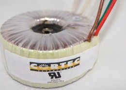 A close up of a toroidal transformer with wires attached to it.