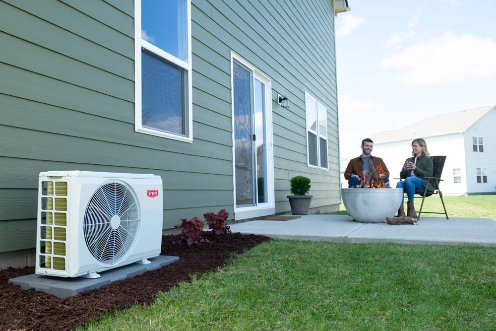 Air conditioner unit next to a house with a couple near a fire pit on a patio.