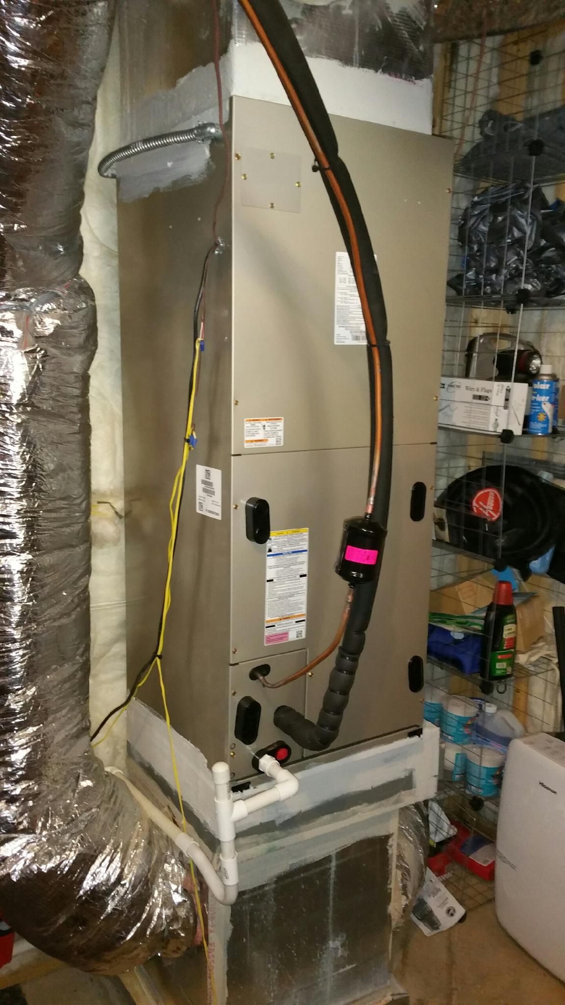 Vertical HVAC unit with ductwork and connected lines in a basement setting.