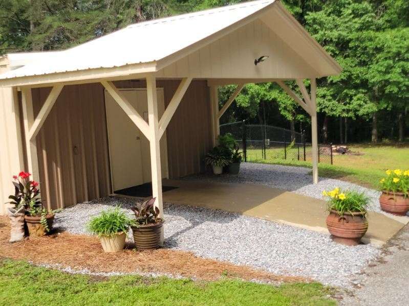 Small tan building with an overhang, gravel pathway, and potted plants.
