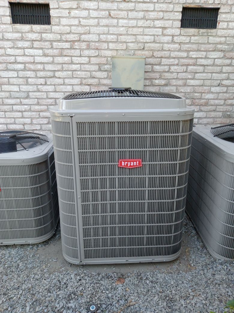 Bryant air conditioning unit with a red logo, standing in front of a brick wall.