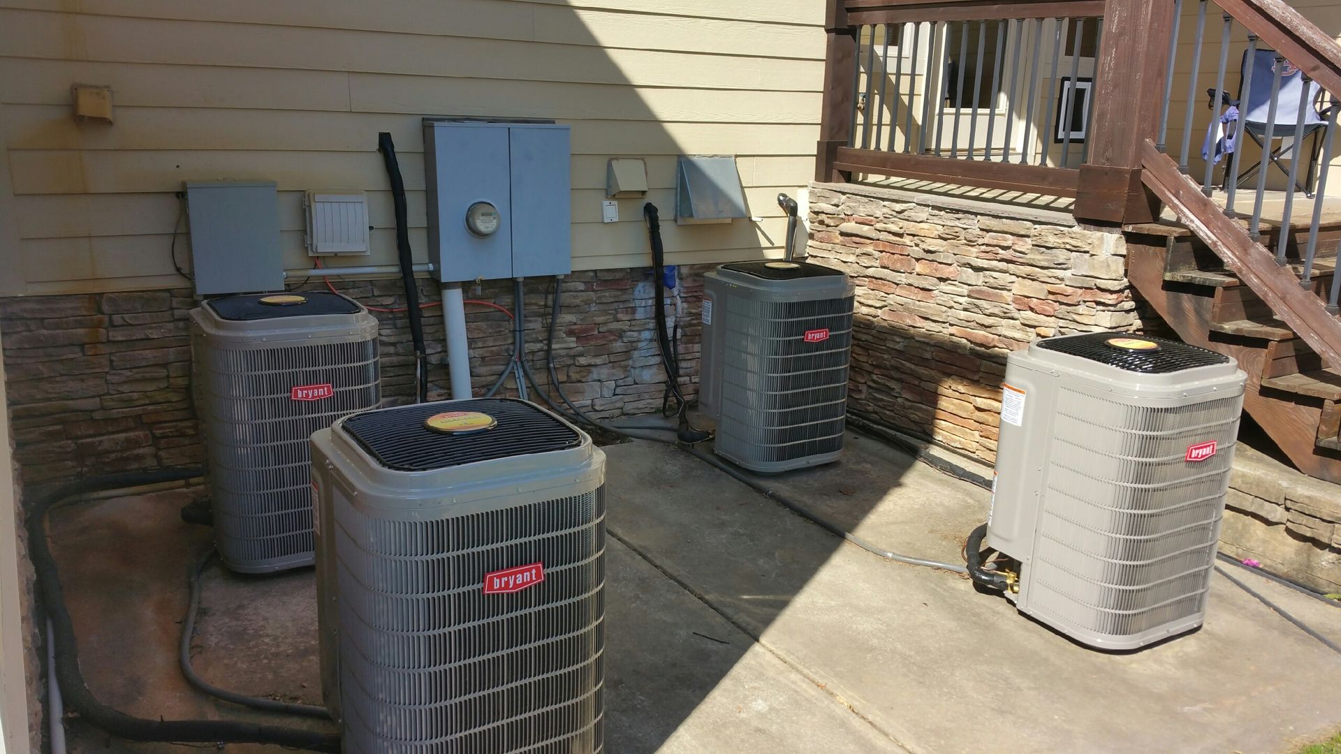 Four Bryant air conditioning units outside, near electrical boxes and a deck.