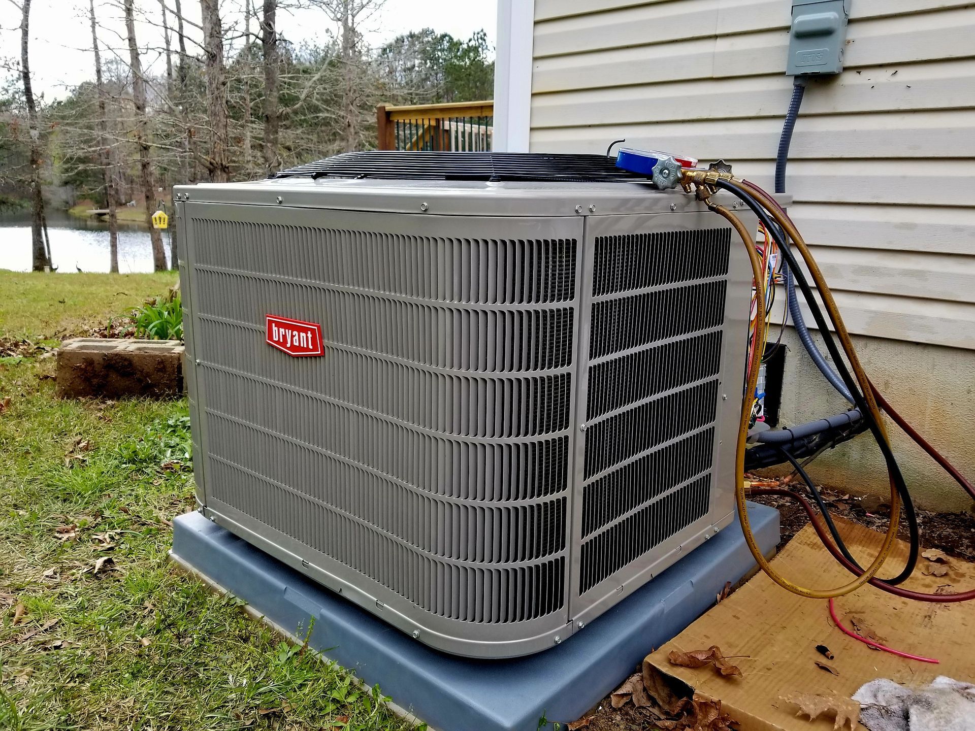 Gray air conditioning unit outside a house, with gauges attached.