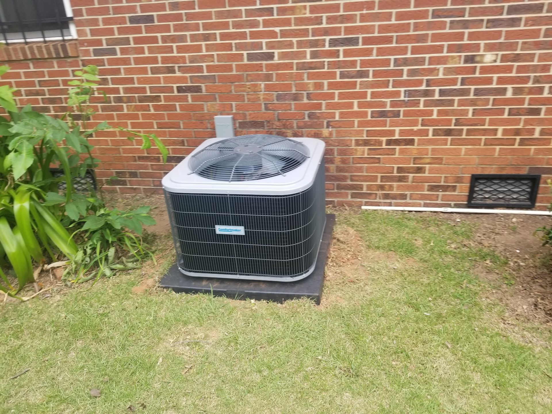 AC unit outside, brick wall background, on black platform, in grass.