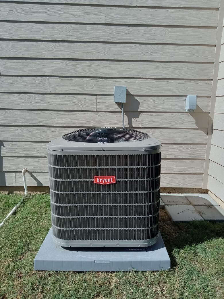 Air conditioning unit outside on a concrete pad, against a gray wall.