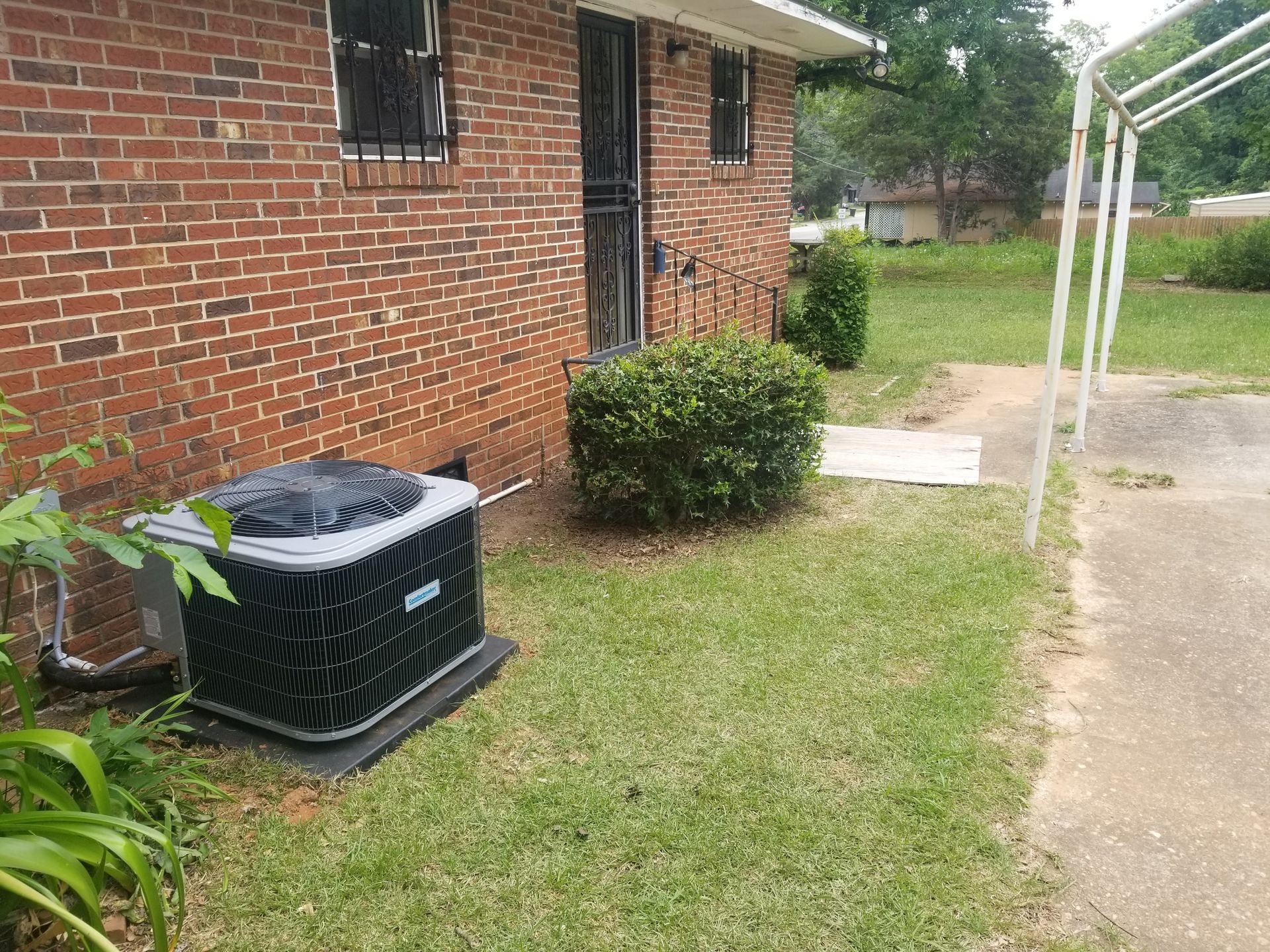 Exterior view of a brick house with an air conditioning unit and a small bush in front.
