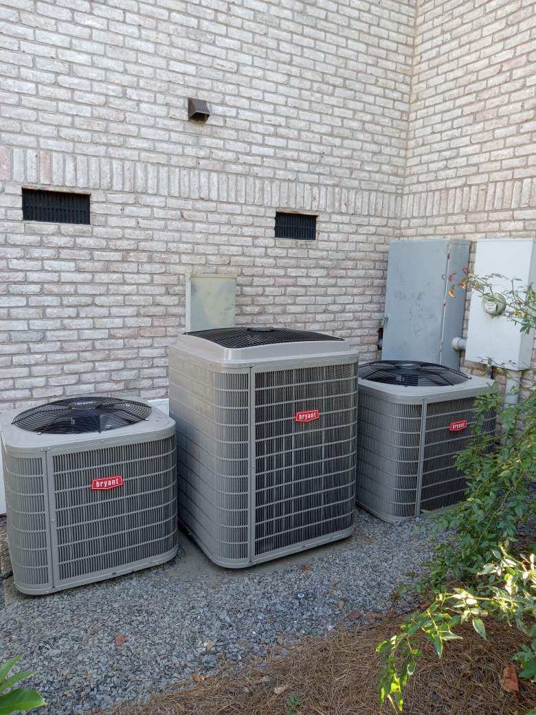 Three air conditioning units against a brick building.