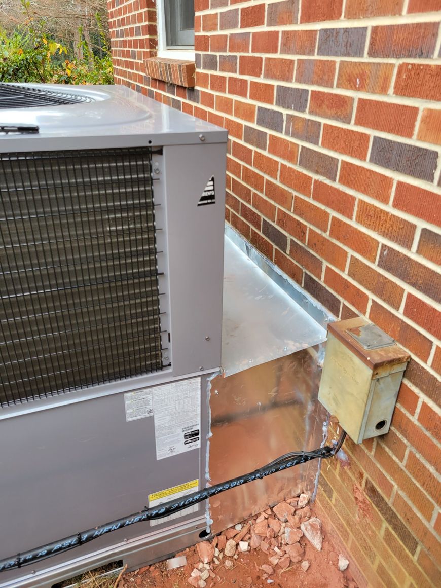 Air conditioning unit next to a brick wall with metal flashing and electrical box.