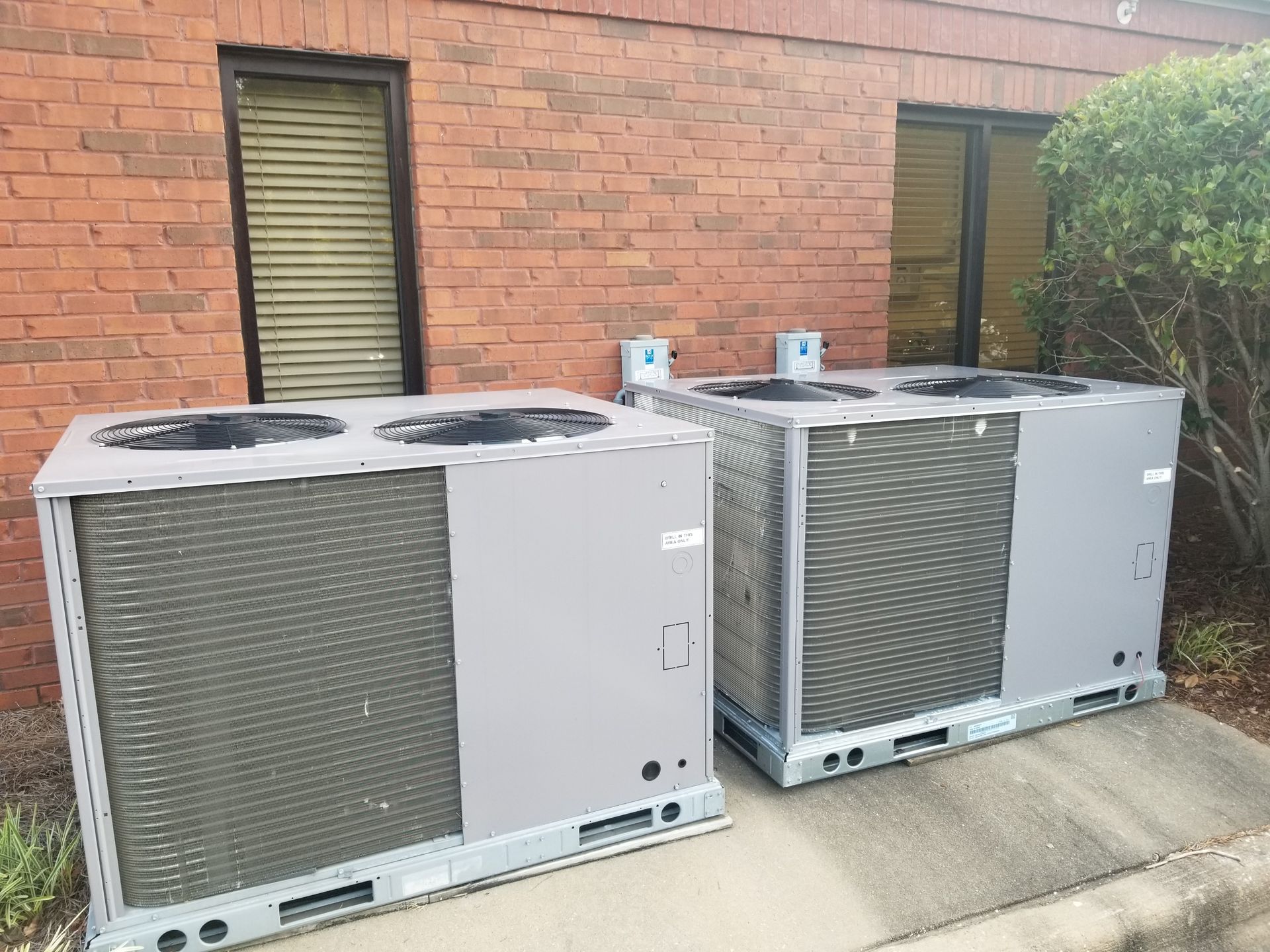 Two large, gray air conditioning units outside a brick building.