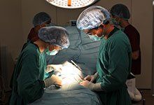 Doctors in green scrubs perform surgery under bright operating room lights.