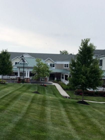 Apartment building with striped lawn, walkway, trees, and a lamppost on a cloudy day