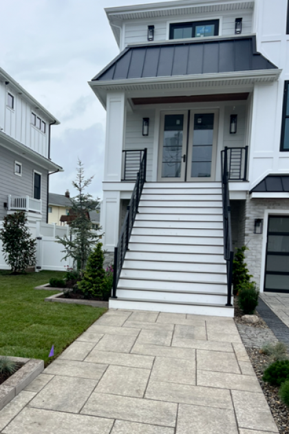 Front entrance of a modern white house with a black awning and stairs up from a stone walkway