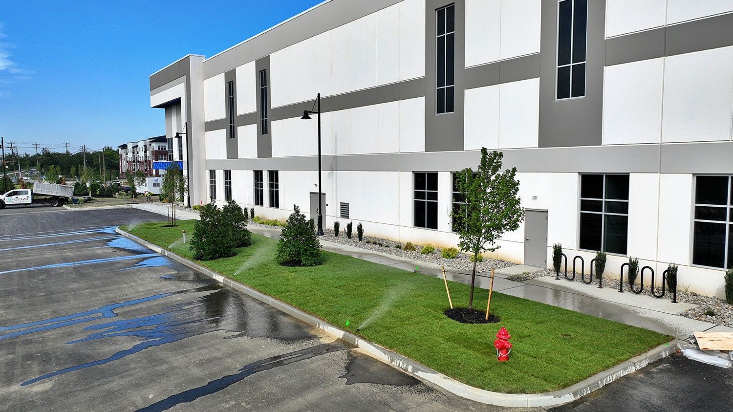 Modern white commercial building with black accents, landscaped lawn, and parking lot under a blue sky