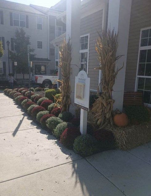 Landscaped apartment entrance with red and green shrubs and a white sign beside the sidewalk