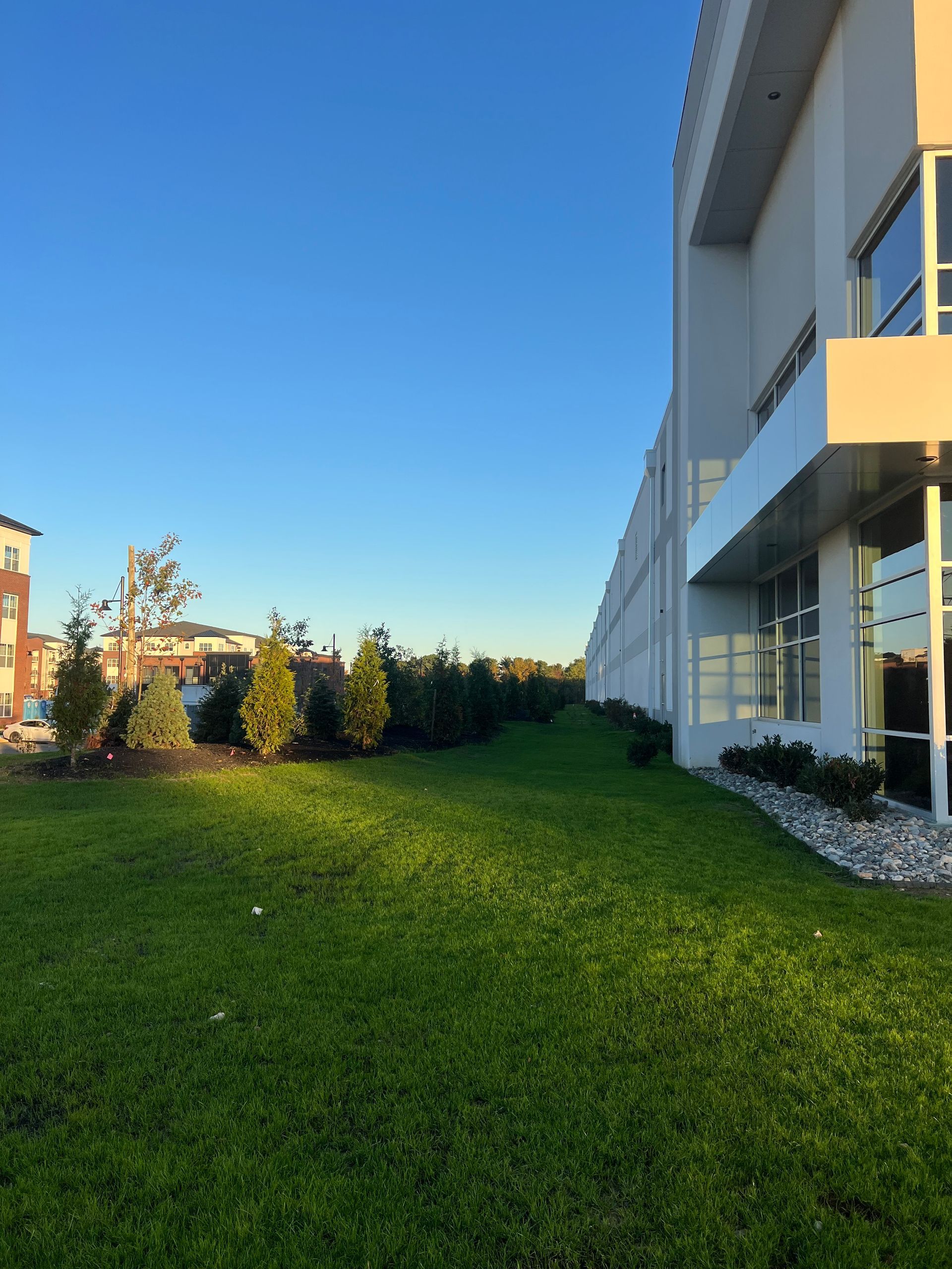 Building exterior with green lawn, shrubs, and a clear blue sky at sunset