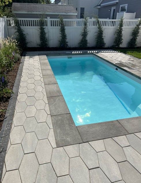 Backyard swimming pool with light stone patio and white privacy fence