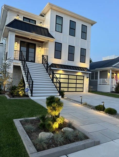 Modern two-story house with front stairs, lit entry, and landscaped walkway at dusk