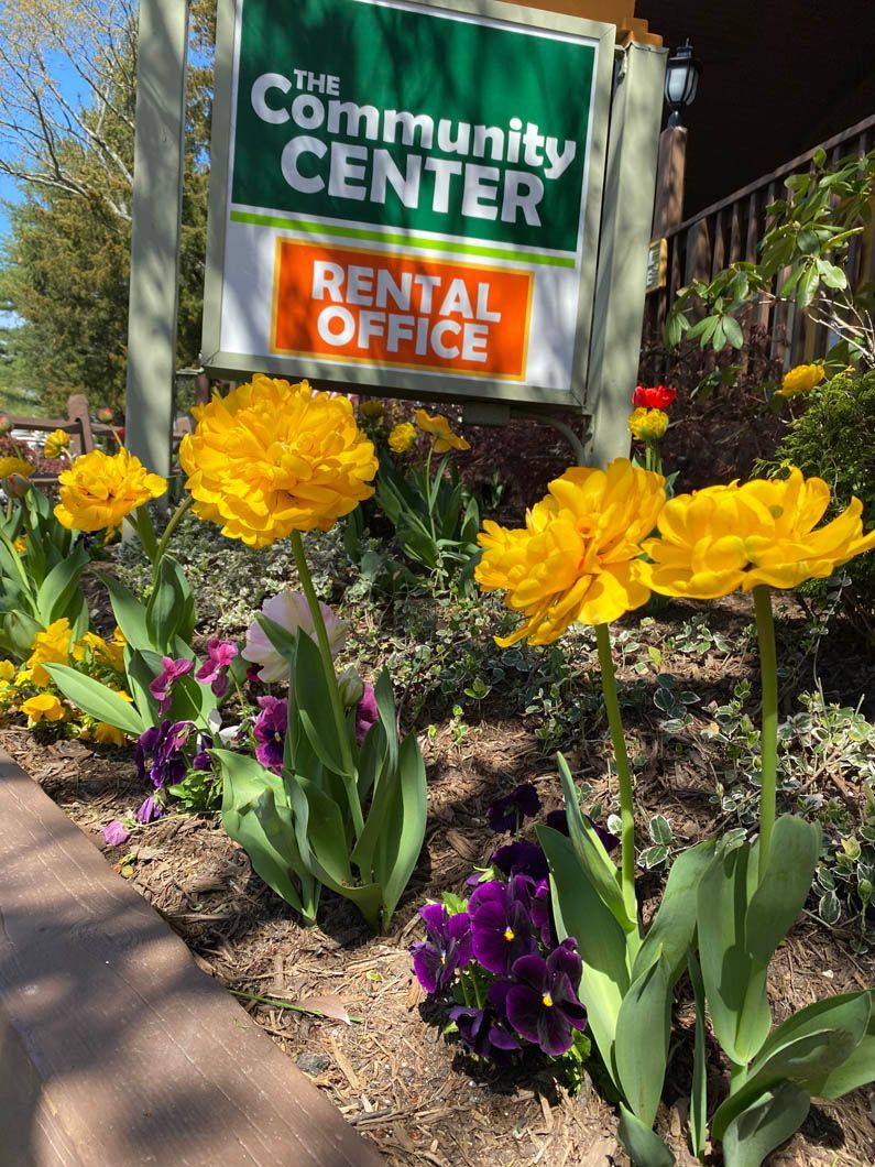Community center rental office sign beside yellow and purple flowers in a landscaped garden