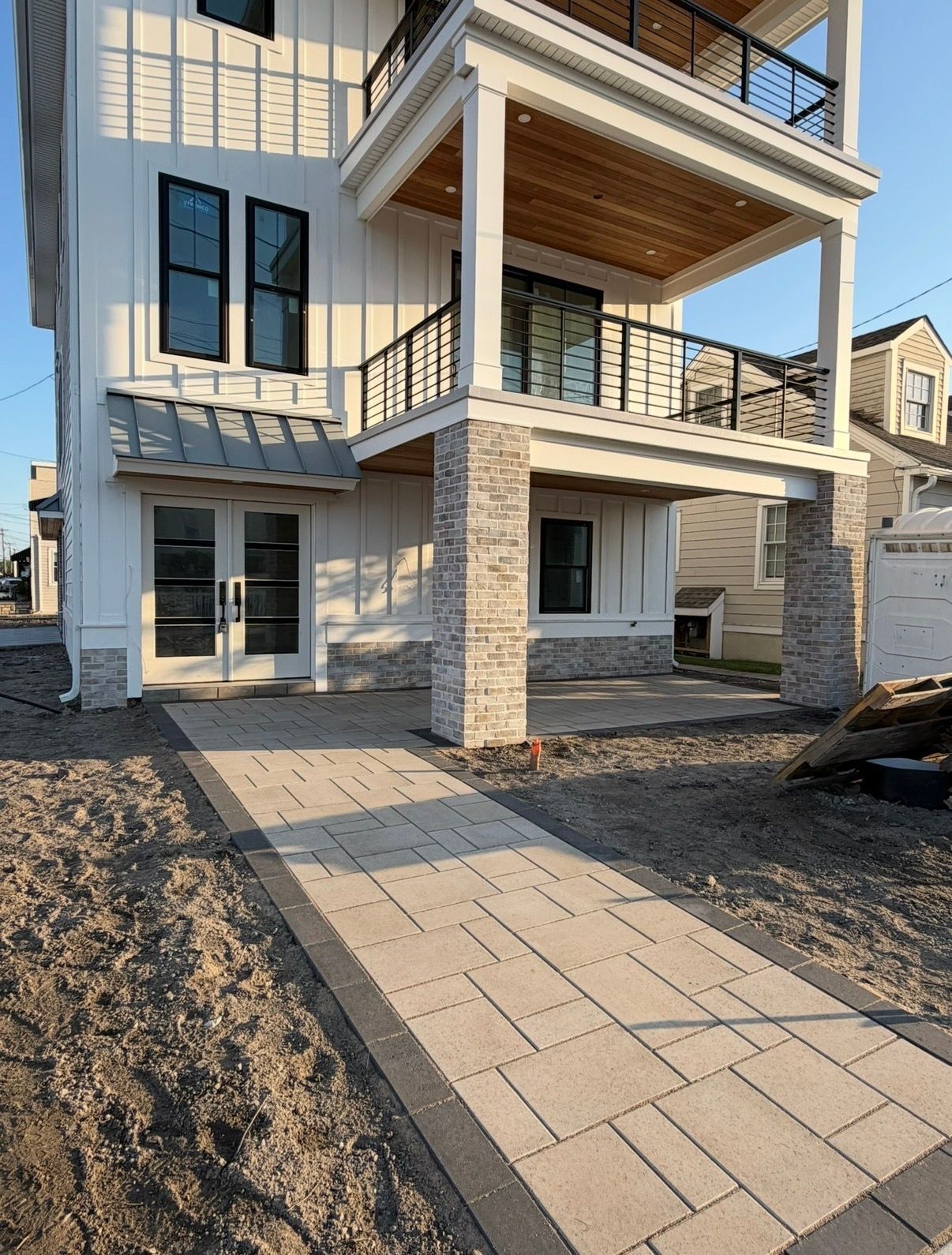 Modern two-story house exterior with stone columns, covered porch, and paved walkway leading to the entrance