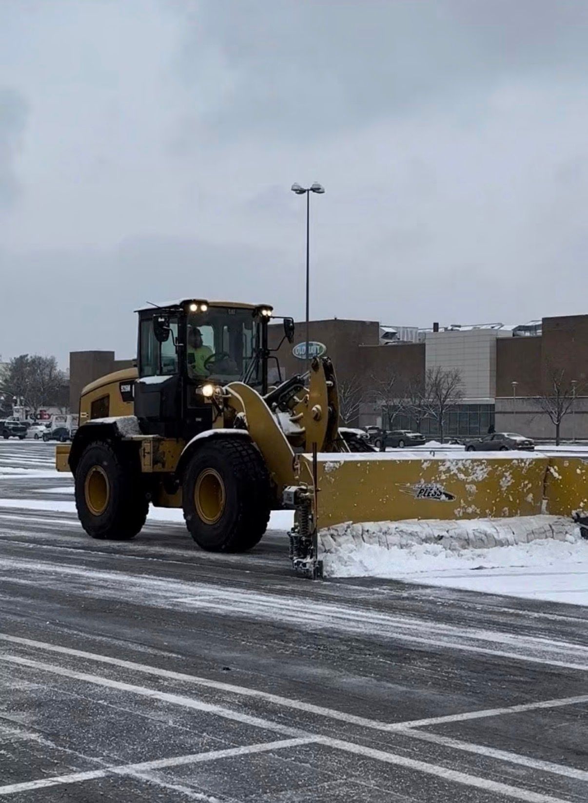 Yellow snowplow clearing a snowy road in a parking lot on an overcast winter day