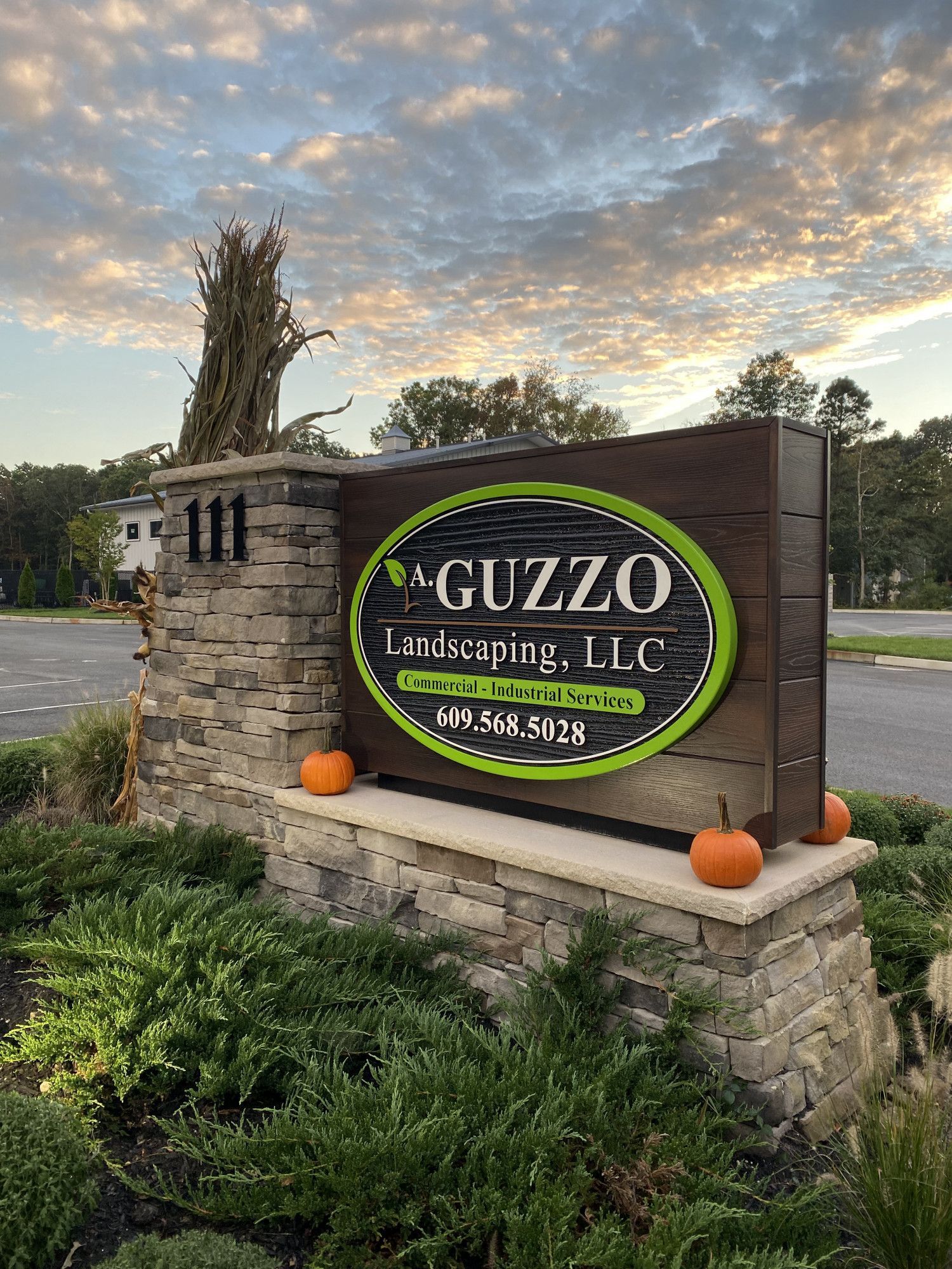 Guzzo Landscaping, LLC sign at dusk with stone wall, pumpkins, and greenery by the roadside