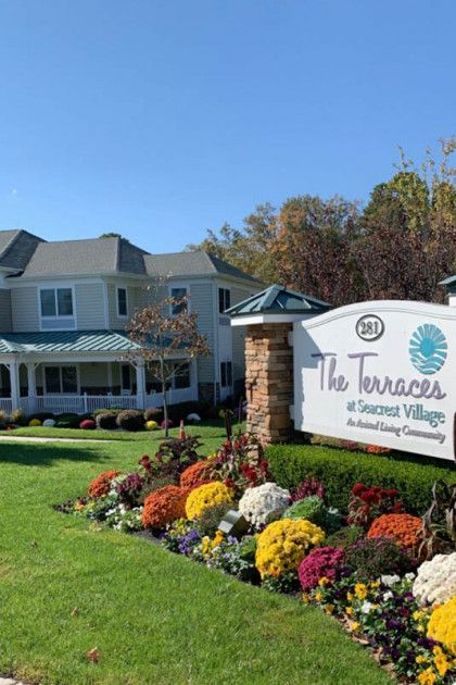 Sign for The Terrace at Sunrise Village beside colorful flower beds and a white building