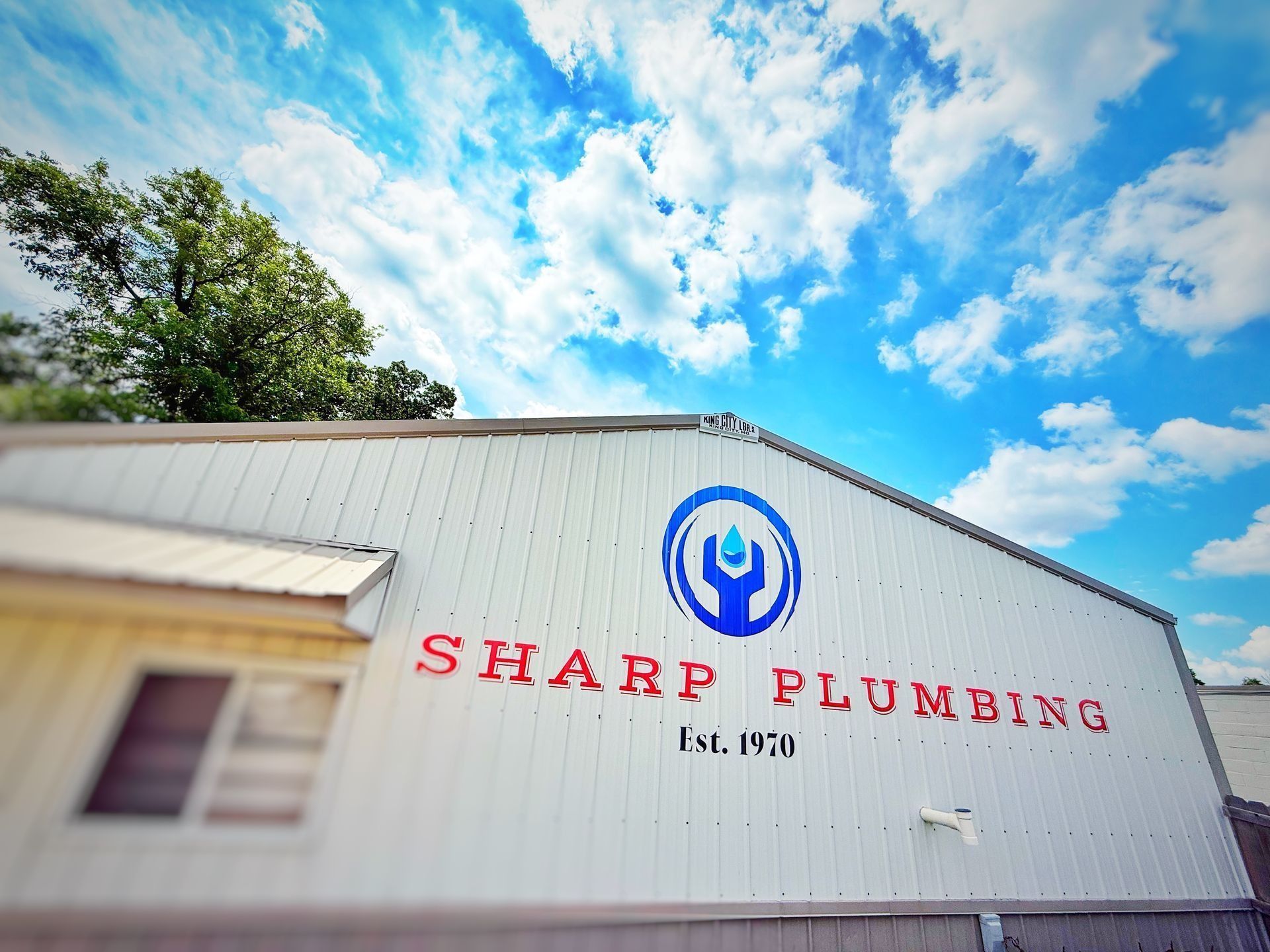 White building with blue logo for Sharp Plumbing, est. 1970, against a bright blue sky.