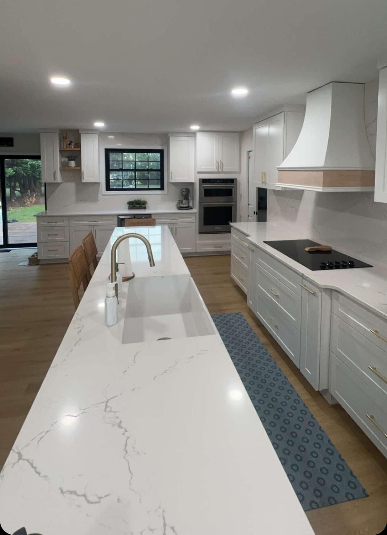 A kitchen with white cabinets , white counter tops , a sink and a stove.