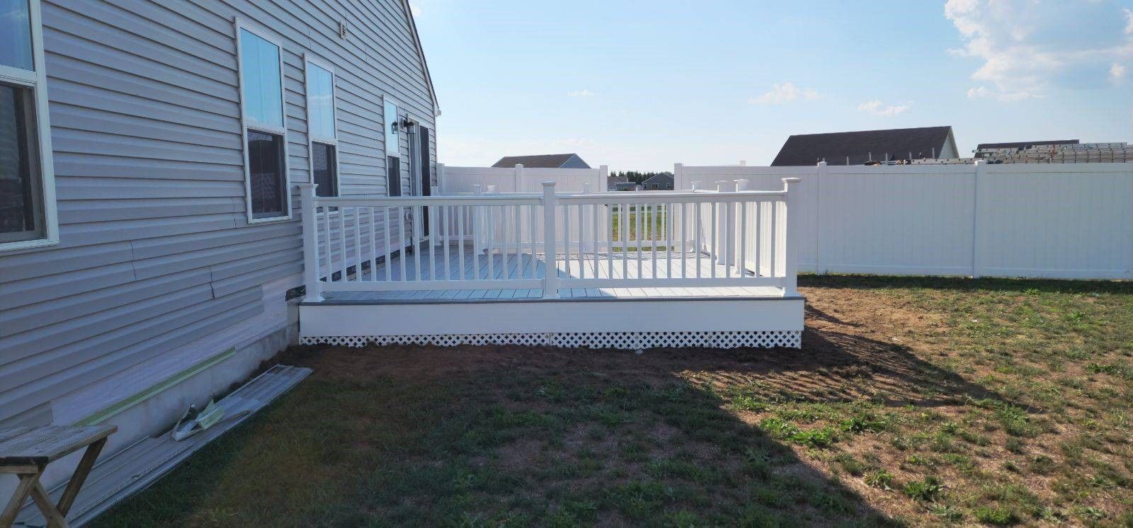 A white deck is in the backyard of a house next to a white fence.