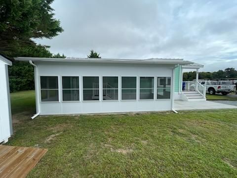 A white house with a screened in porch is sitting on top of a lush green field.