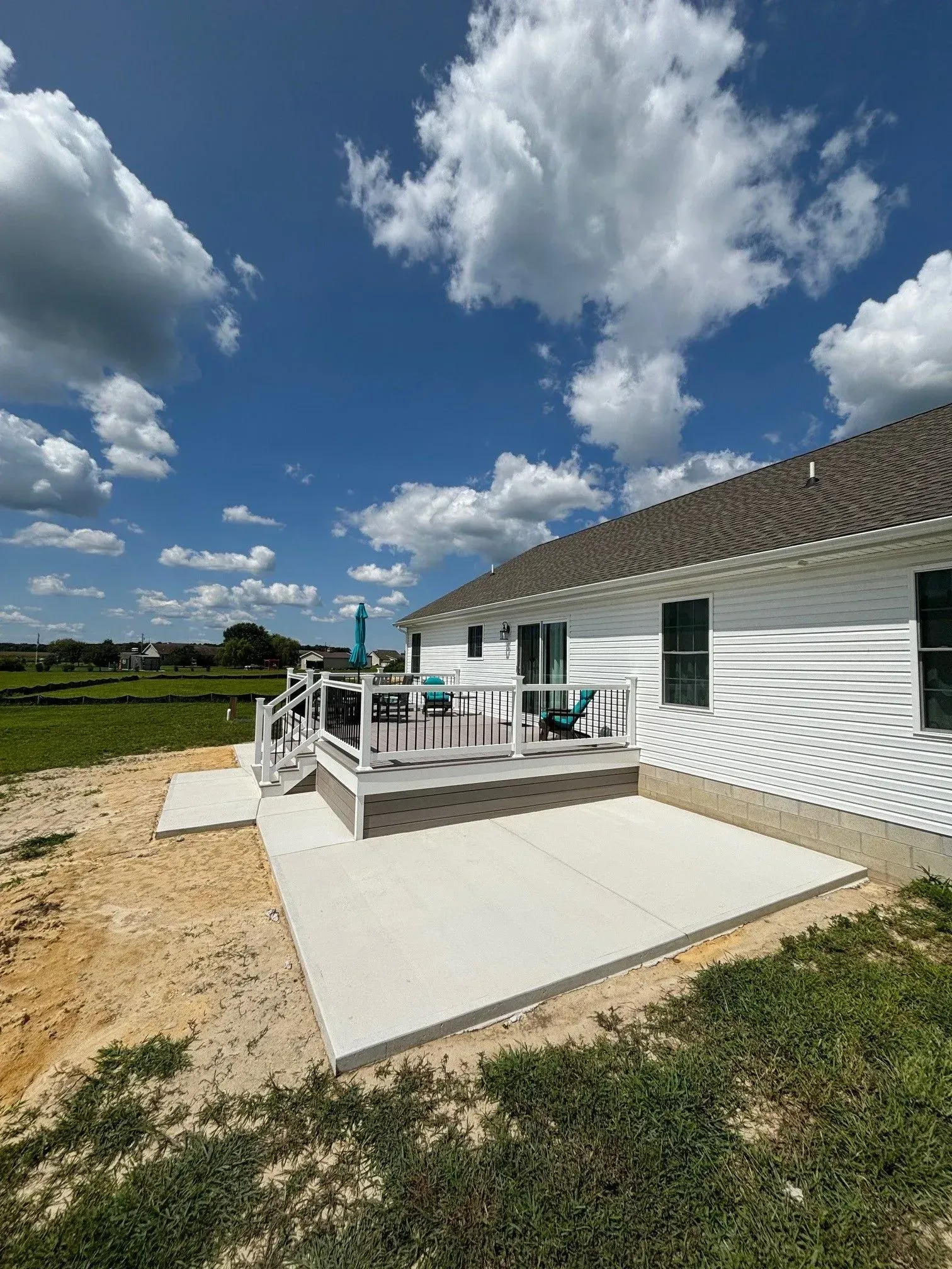 White house with a wooden deck and ramp, set in a sunny rural yard under a blue sky with clouds