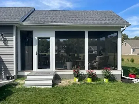 Screened-in patio on a house with white steps, black windows, and potted flowers beside a green lawn.