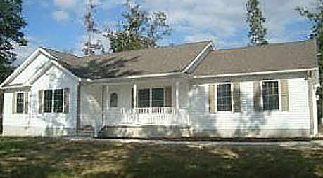 A white house with a brown roof and a porch surrounded by trees.