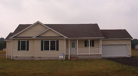 A house with a garage and a porch is sitting in the middle of a grassy field.