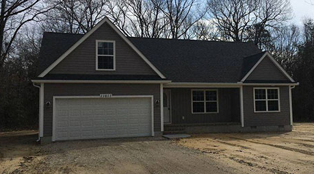 A house with a garage and a gray roof is sitting on top of a dirt road.