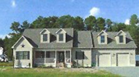 A large white house with a gray roof is surrounded by trees.