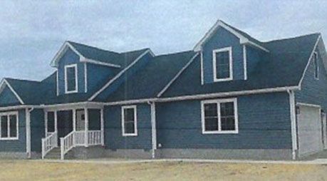 A blue house with a blue roof and white trim is sitting on top of a dirt field.