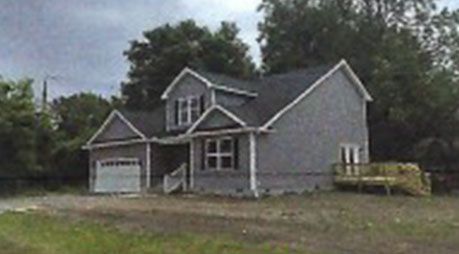 A gray house with a black roof is surrounded by trees.